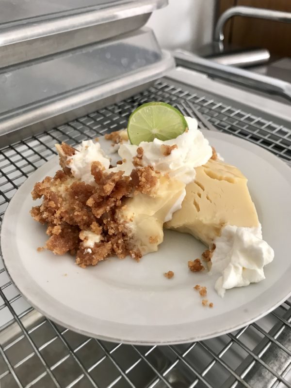 A horribly disfigured piece of key lime pie on a white saucer