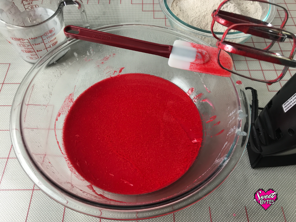 All of the wet ingredients for red velvet cake mixed in a large glass bowl with a spatula balanced on the edge