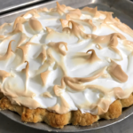 A beautiful lemon meringue pie with a toasted meringues sitting on a baking sheet