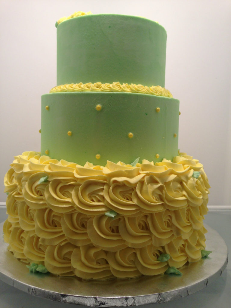 3 tiered green and yellow rosette cake in refrigerator