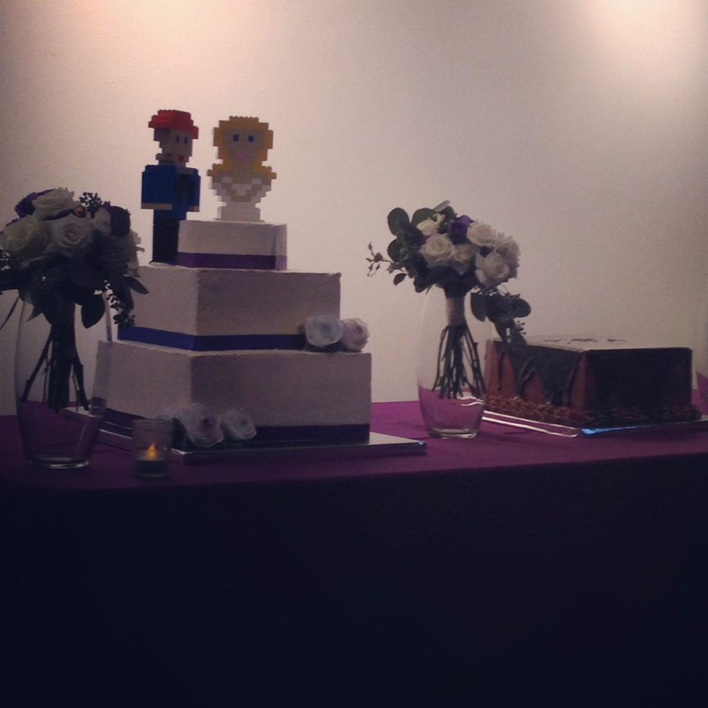 Three Tiered square wedding cake photo taken from a distance. Lego cake toppers on top